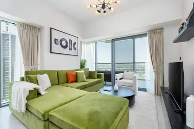 a living room with a green couch and a television at Gala Guests - Golf Gate Residences with Panoramic Golf Views in Dubai