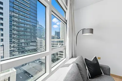 a living room with a couch and large windows at Yacht Bay Tower 1min to Metro, Tram and 5min to Marina in Dubai