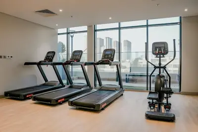 a gym with three treadmills in a room with windows at Bright Studio in Azizi Riviera with Patio & Pool in Dubai
