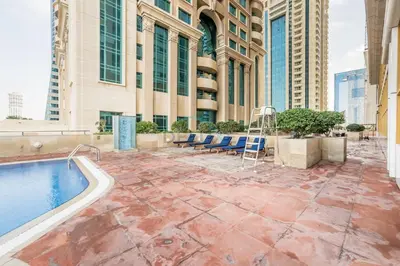 a patio with a pool and chairs and a building at Sky-Level 2BR with Partial Marina View, Just Steps to Dubai Tram and Minutes from the Beach, Elite Residence, Dubai Marina by Deluxe Holiday Homes in Dubai