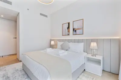a white bedroom with a large white bed and two lamps at 2Bed with spectacular Burj Khalifa & fountain view in Dubai