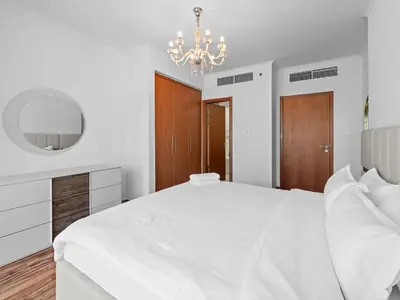 a white bedroom with a large white bed and a chandelier at 1BR in JLT, Steps from Metro, Marina & Mall in Dubai
