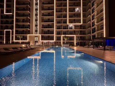 a swimming pool in front of a large building at night at Mahenti - Bright studio near Miracle Garden in Dubai