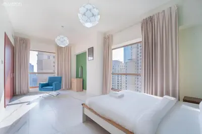 a white bedroom with a large bed and a blue chair at 4BR Spacious Apartment in Sadaf 8 JBR, 3 Min Walk To The Beach With Sea and Dubai Marina View in Dubai