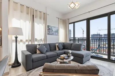 a living room with a couch and a large window at Town Square Zahra 2B - 2 Bedroom Apartment - Allsopp & Allsopp in Dubai