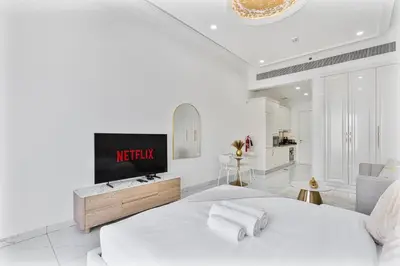 a white bedroom with a television on a bed at Classy Studio APT Close To Dubai Miracle Garden in Dubai