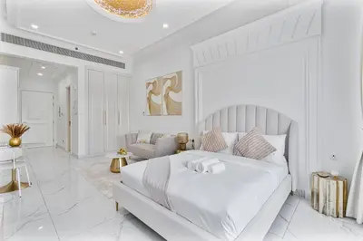 a white bedroom with a bed and a living room at Classy Studio APT Close To Dubai Miracle Garden in Dubai