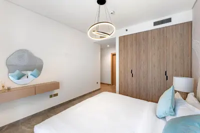 a bedroom with a white bed and a wooden cabinet at Brand New 2BR Peninsula One with Burj Khalifa View in Dubai