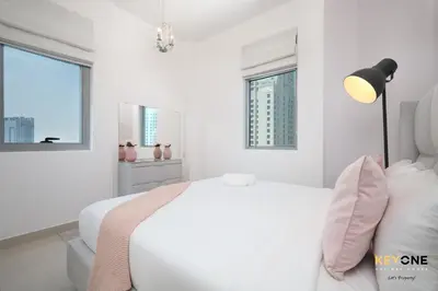 a white bedroom with a bed and two windows at Serene Beachside Two-Bedroom Retreat in Dubai