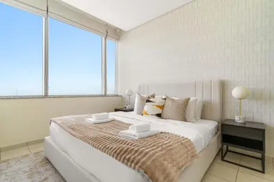 a white bedroom with a large white bed with two tables at Silkhaus Classic 1BDR in DIFC at Sky Gardens in Dubai