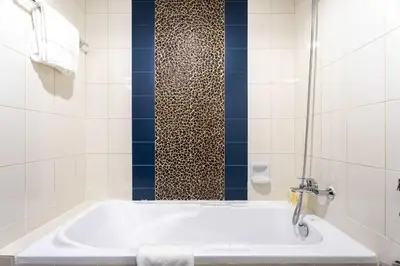 a white bathroom with a tub and a shower at Chic 1BR w Pool Sauna & Steam Room Access in Dubai