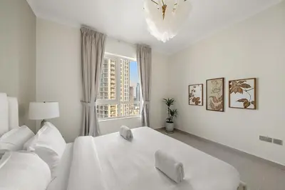 a white bedroom with a large white bed and a window at FIRST CLASS 2BR Burj and Fountain Cozy Luxe in Dubai