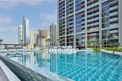 a swimming pool with white chairs and a tall building at Luxury Studio in Peninsula One, Bay Views in Dubai