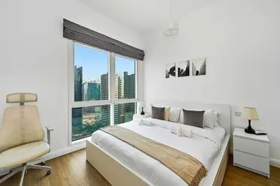 a white bedroom with a bed and a chair and a window at Spacious modern 2 Bed and Maids I Sleeps 7 in Dubai