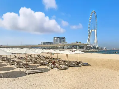 a beach with chairs and a ferris wheel in the background at Prestigious 2BD Seaside Apartment, The Address JBR in Dubai