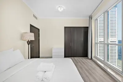 a white bedroom with a large bed and large windows at Torch Dubai Marina 2BDR with Pool Gym and Views in Dubai