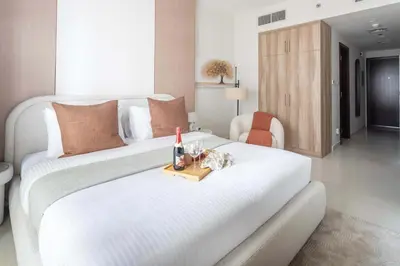 a large white bed with a bottle of wine and glasses at Frank Porter - Hera Tower in Dubai