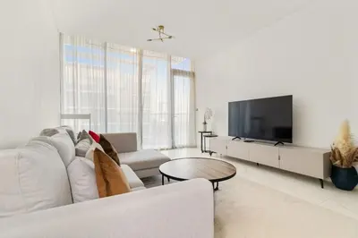 a white living room with a white couch and a tv at Spacious 1BR for 2, 10 Min Meydan Racecourse, Pool & Gym Access in Dubai