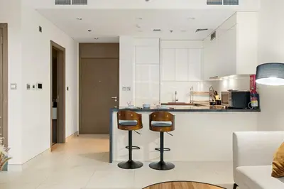 a kitchen with two bar stools in front of a counter at Spacious 1BR for 2, 10 Min Meydan Racecourse, Pool & Gym Access in Dubai