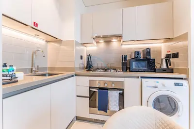 a kitchen with white cabinets and a washer and dryer at Modern Apartment Near Sobha Hartland Amenities, Minutes from Ras Al Khor Wildlife Sanctuary and Downtown Dubai, Sobha Creek Vistas Tower A, Sobha Hartland by Deluxe Holiday Homes in Dubai