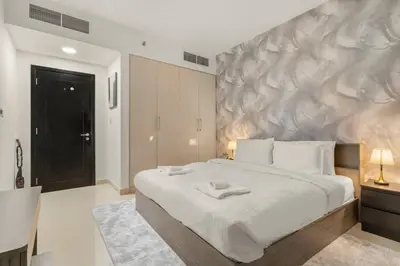 a bedroom with a large white bed with a painting on the wall at Charming 1BR with Balcony and City View in JVC in Dubai