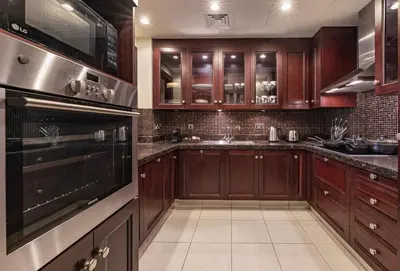a kitchen with wooden cabinets and a stove top oven at Theatre Room - Pool Access - Central 2br Apartment in Dubai