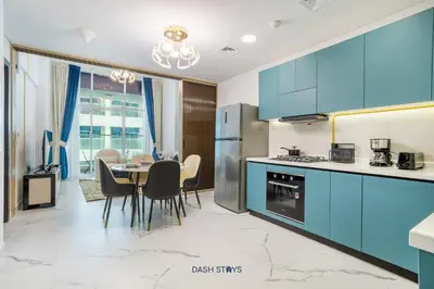 a kitchen with blue cabinets and a table with chairs at Luxury 1BR with 2 Balconies Dubai Science Park in Dubai