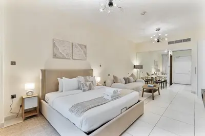 a white bedroom with a large bed and a living room at Elegant Studio on Palm Jumeirah With Stunning Views in Dubai