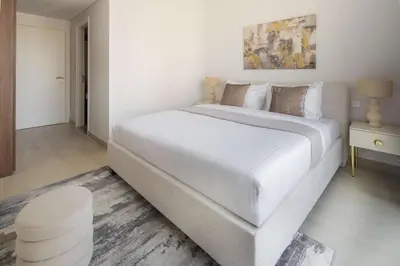 a large white bed in a white bedroom with a stool at Frank Porter - Jadeel 3 in Dubai