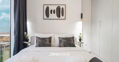 a white bedroom with a bed and a window at Stylish Luxury 1BR - Modern Design - JVC in Dubai