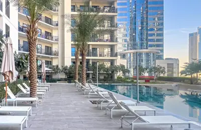 a pool with lounge chairs and palm trees in front of a building at Zada Tower, Business Bay - 1 Bedroom - Allsopp & Allsopp in Dubai