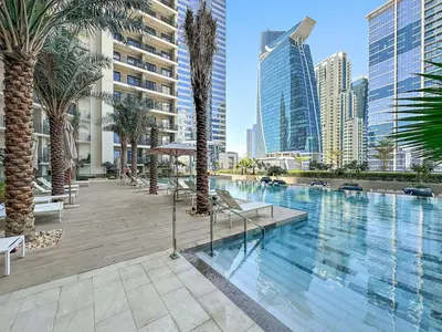 a swimming pool with palm trees and buildings at FIRST CLASS 1BR Pool View & Prime Location in Dubai