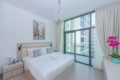 a white bedroom with a bed and a large window at VayK - Brand New 1BR in Dubai Hills in Dubai