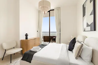 a white bedroom with a large bed and a chair at VayK - Stylish 2BR in JVC with Private Pool in Dubai