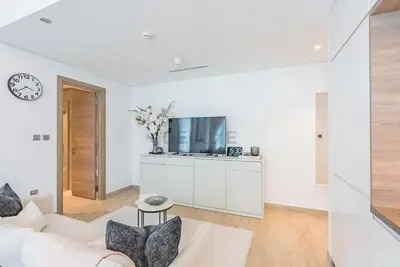 a white living room with a white couch and a tv at Stylish 2BR Stay Near Marina Beach and Ain Dubai, Steps from Shops and Restaurants, Studio One, Dubai Marina by Deluxe Holiday Homes in Dubai