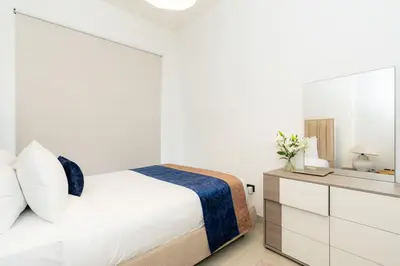 a white bedroom with a bed and a dresser at CitiHome - Modern Stay - Dubai Hills 2BR in Dubai