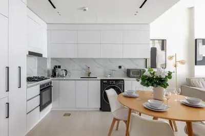 a white kitchen with a wooden table and chairs at Modern 1BR Apartment with City View in Dubai