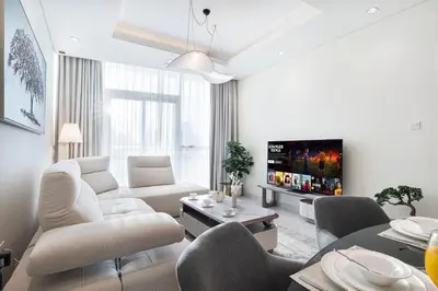 a white living room with a couch and a tv at Maison Distinction Suites by Hostiva - Burj and Fountain View in Dubai