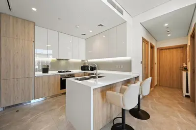 a kitchen with white counters and wooden cabinets at Spacious & Cozy 2BD Apartment Peninsula One, Dubai in Dubai