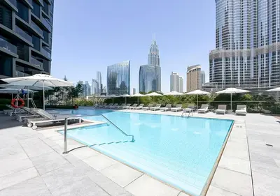 a large swimming pool with chairs and umbrellas in a city at Burj Khalifa & Fountain Sky Suite on The Address Opera in Dubai