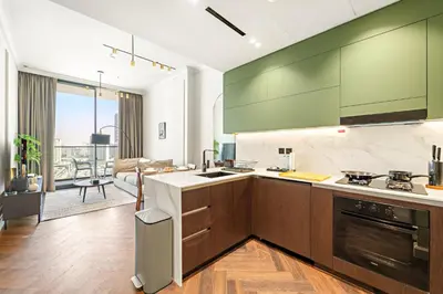 a kitchen with green cabinets and a living room at Modern 1BR Apartments by Nestovia in JVC with Pool and City Views in Dubai