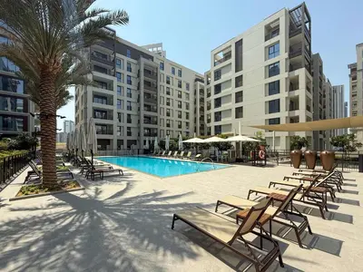 a pool with chairs and a palm tree and buildings at Frank Porter - Rosewater at Creek Beach 3 in Dubai