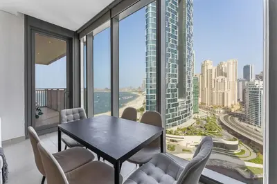 a dining room with a table and chairs and a large window at Beachfront Vibe 2BR APT - Walk to JBR & Bluewaters in Dubai