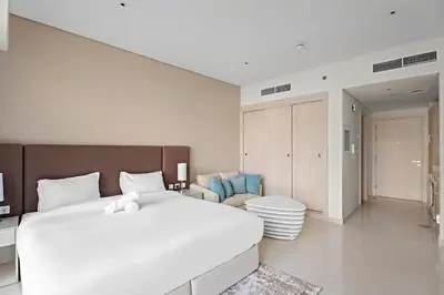 a bedroom with a large white bed and a living room at Stylish Studio with Rooftop Pool on the Palm in Dubai