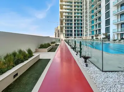 a red walkway next to a building with a swimming pool at Chic Studio with Balcony, Gym & Pools in JVC in Dubai