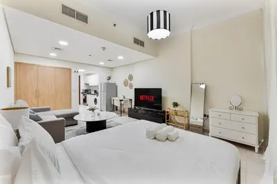 a white bedroom with a large bed and a living room at Splendid Studio near Canal & famous Golf Clubs in Dubai