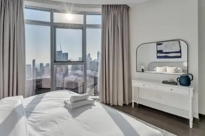 a white bedroom with a large window and a bed at GuestReady - High-Floor 2BR | City and Canal View in Dubai