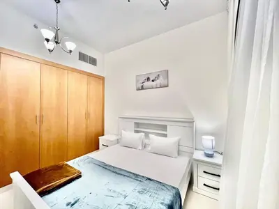 a white bedroom with a bed and a wooden cabinet at Not far from metro Spacious in Dubai