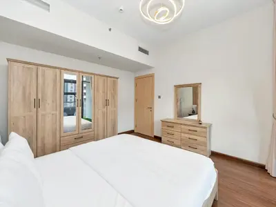 a bedroom with a large white bed and wooden cabinets at Sleek 1BR Apt Free Pool & Gym Access in Dubai