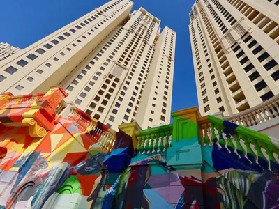 two tall buildings with a colorful mural in front of them at Dubai Beach Living JBR Hostel in Dubai